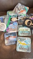 Group view of coasters, bagged mini ships, enamel pins and metal stand