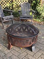 Full view of rusted metal fire pit with mesh lid, chair background