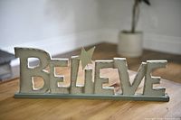 Full view of wooden BELIEVE sign on base