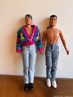 Full view of both dolls standing side by side in outfits