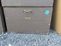 Front view of brown plywood trunk showing brass-tone handle, stencil letters and wear
