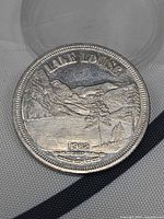 Obverse of 1982 Lake Louise commemorative dollar coin showing mountains, lake, tree, date