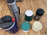 Group shot of six assorted thermoses on wooden floor