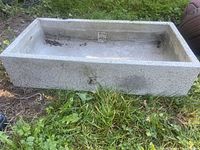 Overall view of concrete rectangular planter resting on grass