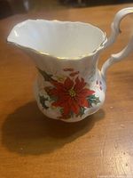 Front view of bone china creamer showing red poinsettia and gold-edged scalloped rim
