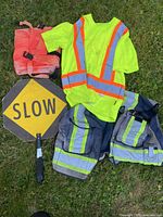All items laid on grass: SLOW paddle sign, hi-vis shirt, vest, pants