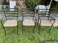 Three black wrought-iron chairs side by side on grass