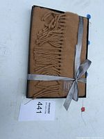 Scarf folded in open gift box showing fringe and tag