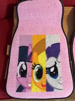 Single car floor mat, pink carpet top with three My Little Pony character faces, black trim visible