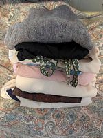 Stack of folded clothing showing grey knit sweater, black blouse, patterned pieces