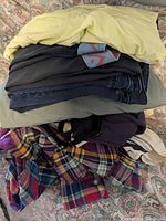 Stacked garments showing yellow T-shirt, dark items beneath, folded jeans, plaid shirt