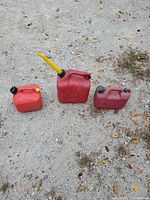 Three red plastic fuel cans displayed on gravel surface