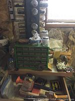 Photo of the green multi-drawer organizer filled with assorted nuts, bolts and small parts, two staplers on top, jars of fasteners in the background
