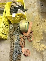 Photo showing assorted tow chains, heavy-duty orange and beige strapping bundled up on concrete floor near yellow crates.