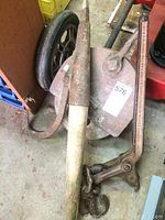 Photo showing metal pulley with hook, steel hauler, and vintage log roller with wooden handle together on floor.