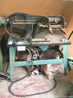 Full view of jointer mounted on green metal bench with power cord visible. Shows condition and structural details of the tool and bench.