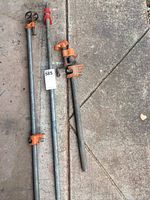 Three metal pipe clamps laid out on concrete. Two longer clamps approximately 35 inches long with orange clamp components, one shorter clamp about 22 inches long.