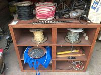 Full view of wooden cabinet with contents: spools of wire, chain, rope, drills, hand tools, and hardware.