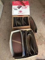 First box opened showing rolled sanding belts inside. The box label reads 'Rouleau économique Toile Alumine 1 1/2 x 50’ with branding and product details.