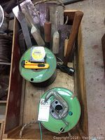 Wooden box containing two large reels of electrical wire, a Stanley tape measure, and a yellow box cutter on top.