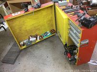 Open view of wooden chest showing contents: electrical supplies, wire connectors, tools and power cords inside and on top.