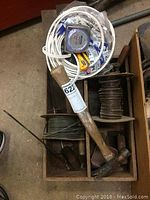 Top view of wooden box containing hammer, rolls of electrical wire, measuring tape, and various hand tools.