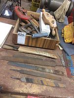 Photo showing a wooden box containing C-clamps, a wooden hand plane, and other small woodworking tools, with several metal rasps and files laid out on the table in front of it.