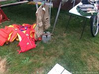 Photo showing multiple red and yellow youth life jackets, fishing vests hanging on a pole, green tackle box on table, and bicycle frame partially visible.
