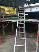Ladder leaning against a raised platform outdoors, showing full length and environment.