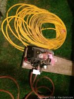 Full view of yellow coiled hose with pump unit on wooden pallet in grass.
