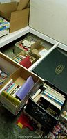 Boxes and containers filled with assorted books showing the overall quantity and variety in the lot.