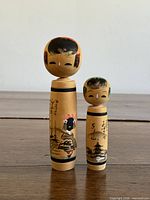 Front view of both kokeshi dolls showing painted scenes and calligraphy