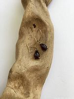 Both earrings displayed on driftwood showing overall design, hooks, and garnet settings