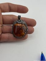 Front view of sterling silver pendant showing amber cabochon and floral top