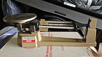 Left side view of complete OHAUS triple beam balance showing pan, beam, base, and sliding weights