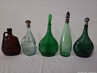 Front view of all five glass bottles lined up showing colors, shapes and stoppers