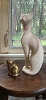 Large off-white ceramic cat and small brass cat on table