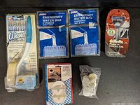 All six items laid out including Hard Water Wand, two emergency water bags, Park-A-Plug set, bag of stoppers, and Gillette razor pack