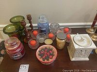 Various Yankee brand candles in jars and bowl, wooden candle holders, glass votive candle holders with candles, and ceramic candle warmer on a wooden table.