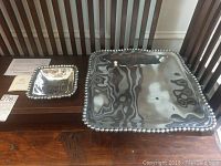 Two square silver plated Lenox pieces on wooden chair with use and care instructions visible. Larger platter 16x16 inches and smaller dish 6x6 inches shown side by side.