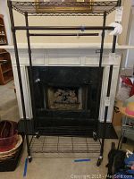 Full view of the bronze aluminum rack with wire shelves and wheels, positioned in front of a fireplace.