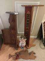 Photo showing two wooden racks leaning against the wall with a cloth doll standing in front and the wooden angel tray on the floor.