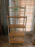 Front view of the full bakers rack showing the four natural wood shelves attached to the white painted frame with horizontal rails and a curved top rail.
