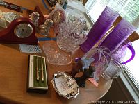 Photo showing purple plastic pitcher, 12 matching glasses, crystal basket, boxed Cross pens, silver plated bowl, salt and pepper shakers, and nativity figurines on table.