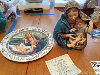 The collectible plate and Madonna statue displayed next to each other on a table with their certificate of authenticity.