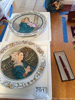 Two decorative plates and a boxed pen arranged on a table.
