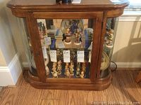 Curio cabinet filled with collectible figurines showing front glass door and curved side panels, highlighting the wood finish and glass shelf inside.