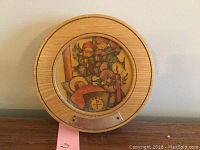 Front view of the round wooden music box showing circular Hummel artwork depicting angel musicians and baby under a glass cover.