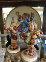 Two porcelain Hummel figurines and a decorative collector plate displayed together