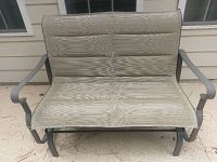 Front view of two-seat glider bench with beige mesh fabric and dark metal frame, placed outside on porch.